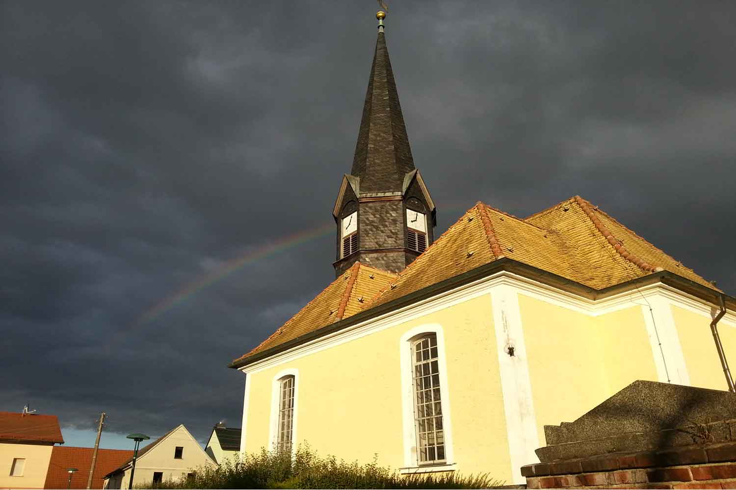 Kirchturm mit Regenbogen und Uhr